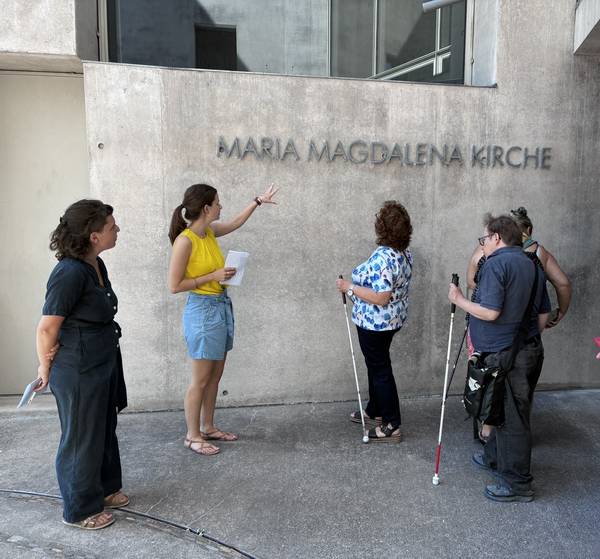 Blinde und sehende Menschen stehen vor dem tastbaren Schriftzug der Maria-Magdalena-Kirche in Freiburg/Rieselfeld.